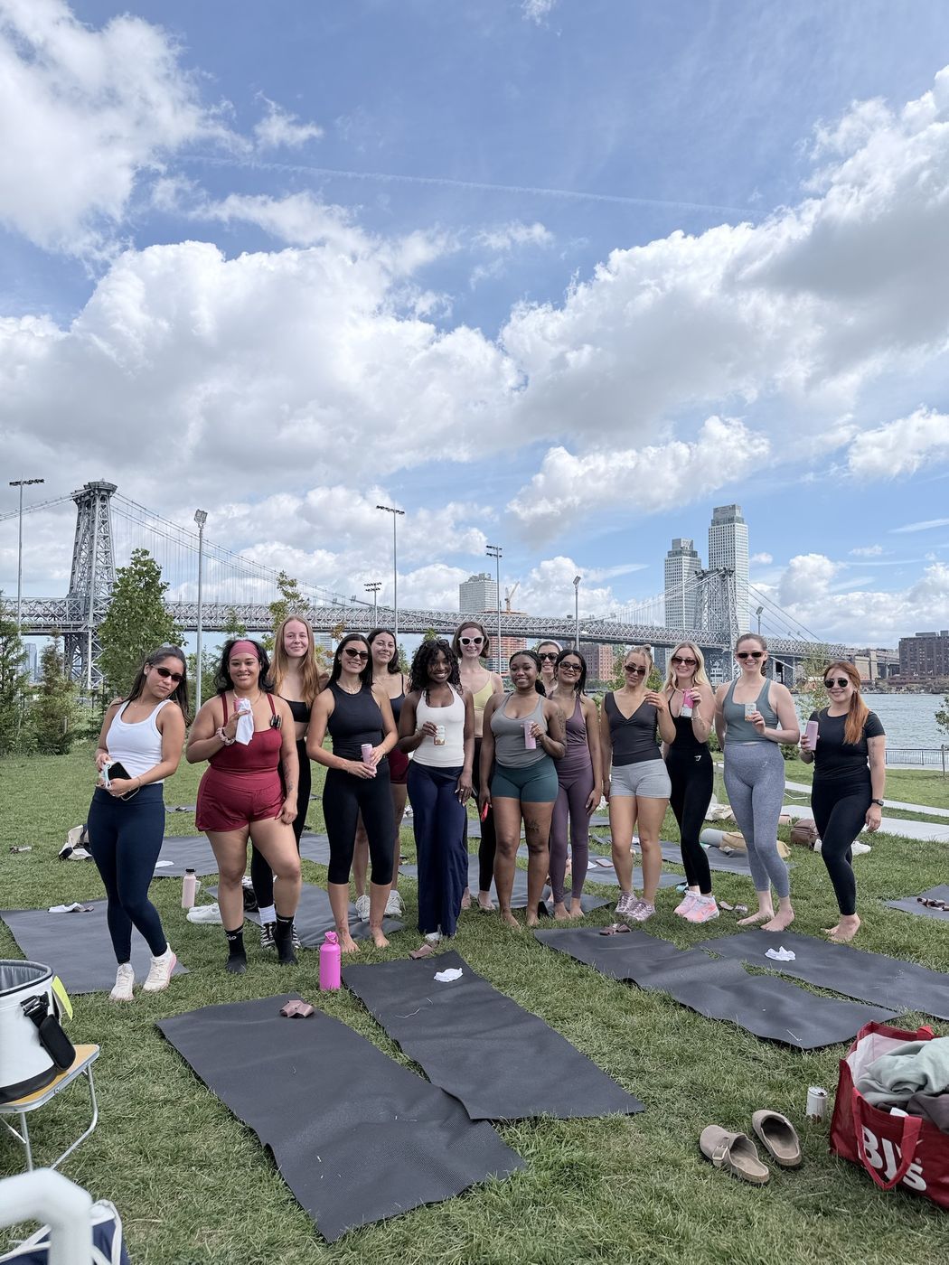 A SYNC group on the grass by the East River, the Williamsburg Bridge behind them